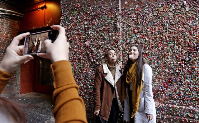 Natalia Stratton, left, and Sarah Santee pose for their friend as they blow bubble gum bubbles while standing at the landmark “gum wall” in Post Alley at the Pike Place Market Tuesday, October 31, 2017, in Seattle. First cleaned in 2015 after 20 years of collecting gum stuck there by locals and tourists, the wall is now cleaned annually. The gum stuck there now collected in the last six weeks. (Photo by Elaine Thompson/AP Photo)