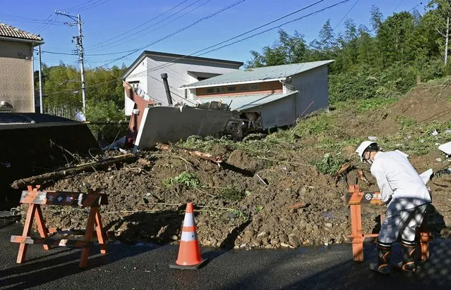 A worker places a barricade at the scene of a landslide that damaged a residential area in Hamamatsu of the Shizuoka prefecture, central Japan, Saturday, September 24, 2022. Tropical Depression Talas unleashed fierce rainfall Saturday in parts of Japan, setting off landslides, halting trains and killing a man after he crashed his car into a pond. (Photo by Mizuki Ikari/Kyodo News via AP Photo)
