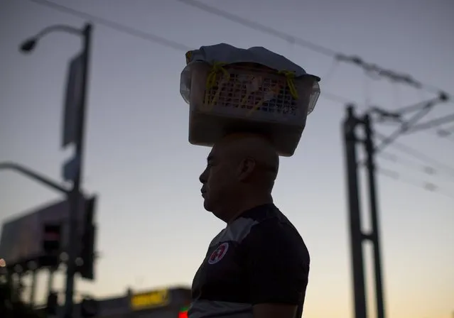 A man crosses the street with a basket of candies balanced on his head in the border town of San Ysidro, California September 3, 2015. (Photo by Mike Blake/Reuters)