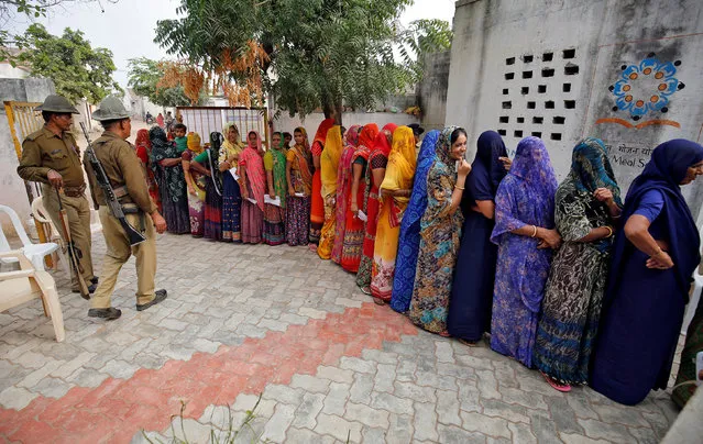 Policemen stand guard as women wait in a queue to cast their votes at a polling booth during the first phase of state assembly election in Devpur village of Surendranagar district in Gujarat, India, December 9, 2017. (Photo by Amit Dave/Reuters)