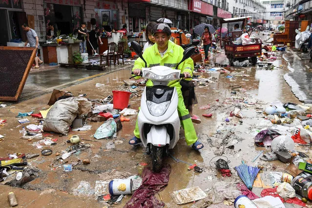 This photo taken on July 7, 2020 shows a man riding a scooter passing a street after heavy rains caused flooding in Shexian county, Huangshan city, in eastern China's Anhui province. (Photo by AFP Photo/China Stringer Network)