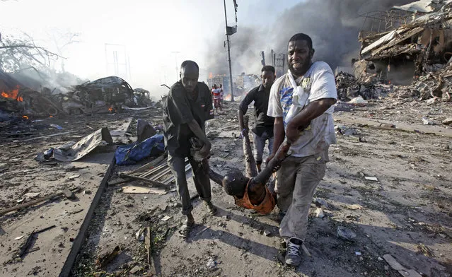 Men remove the body of a man killed in a blast in Somalia's capital Mogadishu on October 14, 2017. The huge explosion from a truck bomb killed at least 20 people and shaken residents called it the most powerful blast they'd heard in years. (Photo by Farah Abdi Warsameh/AP Photo)
