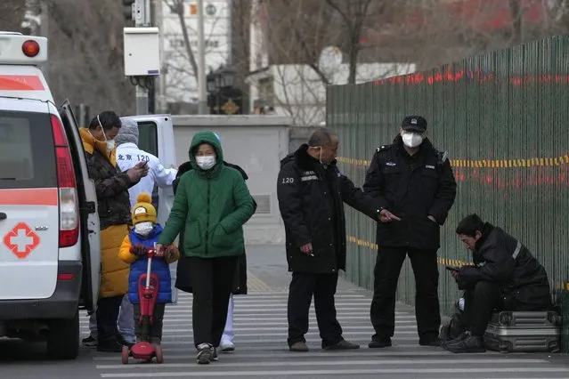Chinese police personnel check on a man who appears unwell and resting on top of his luggages on the street of Beijing, Friday, December 30, 2022. China is on a bumpy road back to normal life as schools, shopping malls and restaurants fill up again following the abrupt end of some of the world's most severe restrictions even as hospitals are swamped with feverish, wheezing COVID-19 patients. (Photo by Ng Han Guan/AP Photo)