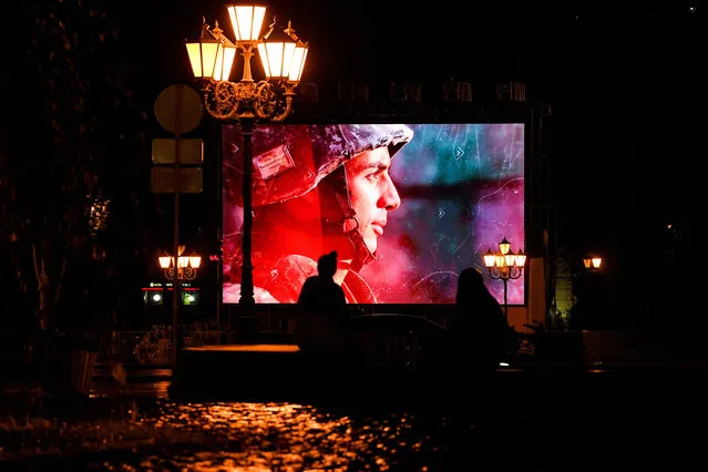 People walk in front of a big screen displaying military patriotic videos in Yerevan on October 5, 2020, during the ongoing fighting between Armenia and Azerbaijan over the breakaway Nagorno-Karabakh region. (Photo by AFP Photo/Stringer)