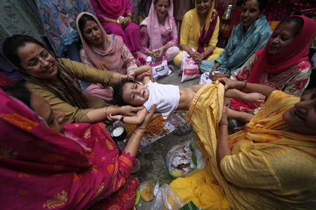 Hindu women belonging to the Dogra community swing a child as part of a ritual as they pray for the long life of their sons during Bacch Dua festival in Jammu, India, Tuesday, August 19, 2025. (Photo by Channi Anand/AP Photo)