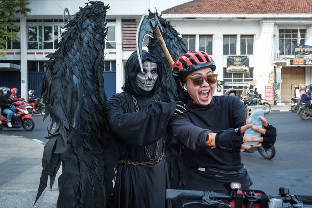 A street performer named Maradona, dressed up as the Grim Reaper, poses with a cyclist in Bandung, West Java, Indonesia on May 4, 2024. (Photo by Yasuyoshi Chiba/AFP Photo)