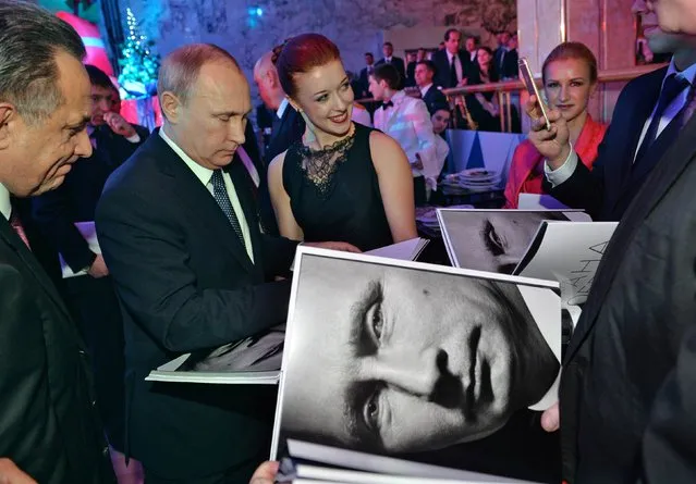 Russian President Vladimir Putin (2nd L) signs autographs on a photo book after a New Year reception in Moscow's Kremlin, December 26, 2014. (Photo by Alexei Druzhinin/Reuters/RIA Novosti)