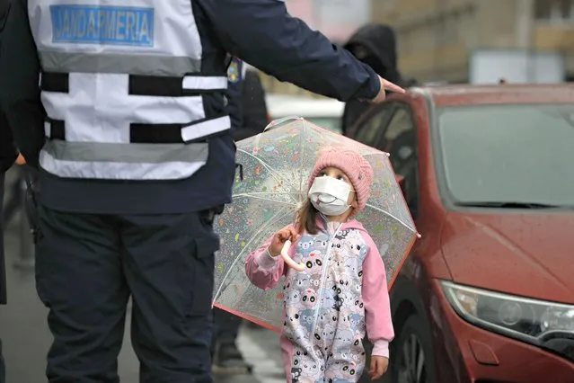 A riot policeman gestures at a little girl during a protest by police unions in Bucharest, Romania, Monday, March 1, 2021. Dozens of Romanian policemen gathered outside the Labor and Social Protection Ministry in protest of planned austerity measures that envisage freezing of salaries in the public sector. (Photo by Vadim Ghirda/AP Photo)