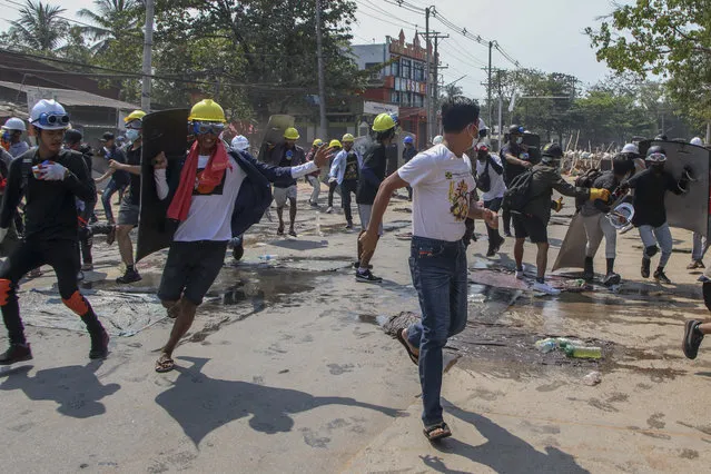 Anti-coup protesters retreat from the frontlines after riot policemen fire sound-bombs and rubber bullets in Yangon, Myanmar, Thursday, March 11, 2021. (Photo by AP Photo/Stringer)