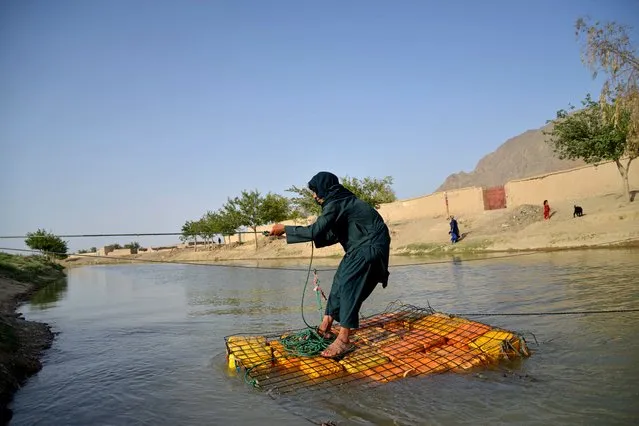 An Afghan youth uses plastic cans to cross a canal in Arghandab district of Kandahar province on June 20, 2023. (Photo by Sanaullah Seiam/AFP Photo)