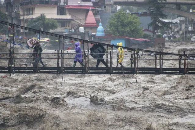 People walk through a bridge across River Beas swollen due to heavy rains in Kullu District, Himachal Pradesh, India, Monday, July 10, 2023. Scientists have long warned that more extreme rainfall is expected in a warming world. (Photo by Aqil Khan/AP Photo)