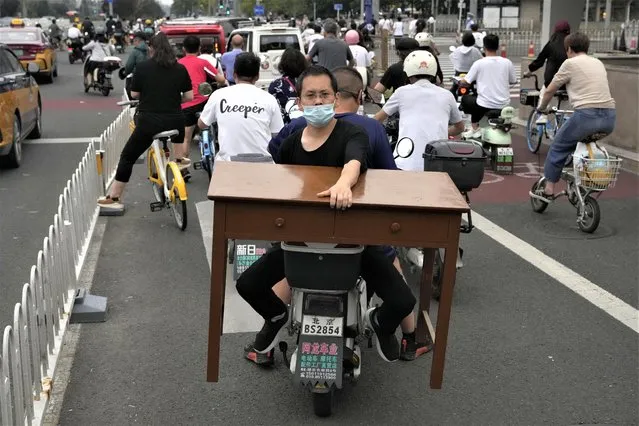 A man holds onto a table while on a bike in Beijing, Thursday, July 27, 2023. (Photo by Ng Han Guan/AP Photo)