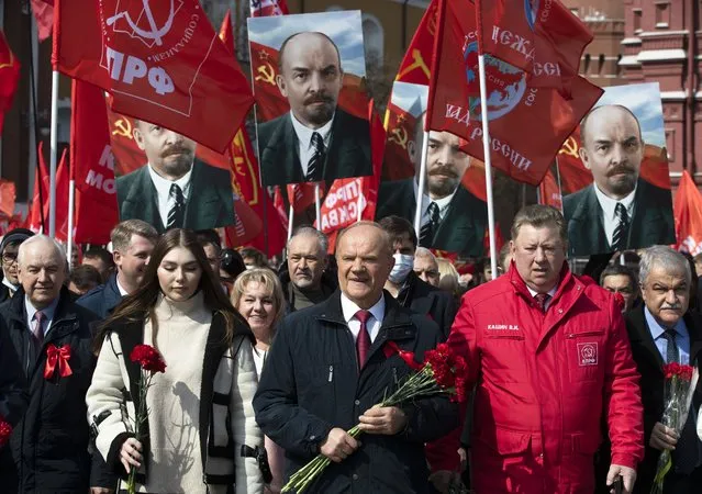 Russian Communist Party leader Gennady Zyuganov, center, and communist supporters hold their flags and portraits of Vladimir Lenin as they walk to visit the Mausoleum of the Soviet founder Vladimir Lenin to mark the 151st anniversary of his birth, in Moscow, Russia, Thursday, April 22, 2021. (Photo by Pavel Golovkin/AP Photo)