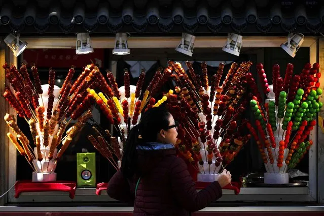 A woman buys a sugar-coated haws stick from a store on a street in Beijing, Thursday, December 29, 2016. Sugar-coated haws, also known as “Tanghulu” is a traditional Chinese candied snack popular in northern China, especially in Beijing during the winter season. (Photo by Andy Wong/AP Photo)