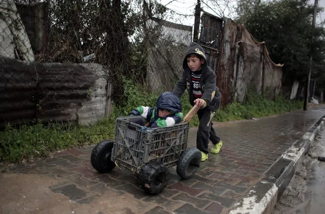 A Palestinian boy uses a homemade wagon made from a plastic crate to wheel his brother during a rainy day in Jabaliya Refugee Camp, southern Gaza Strip, Sunday, February 7, 2016. (Photo by Khalil Hamra/AP Photo)
