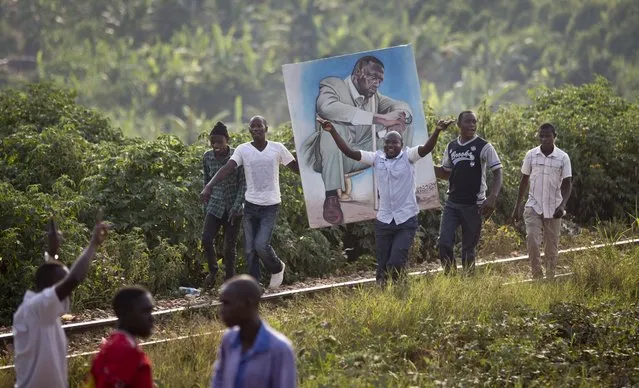 Supporters carry a painting of opposition leader Kizza Besigye as they walk along train tracks to get to an election rally on the outskirts of Kampala, Uganda Sunday, February 14, 2016. Ugandans go to the polls on Thursday, and opinion polls have showed the race tightening between long-time President Yoweri Museveni and Kizza Besigye, the opposition leader who is his closest challenger. (Photo by Ben Curtis/AP Photo)