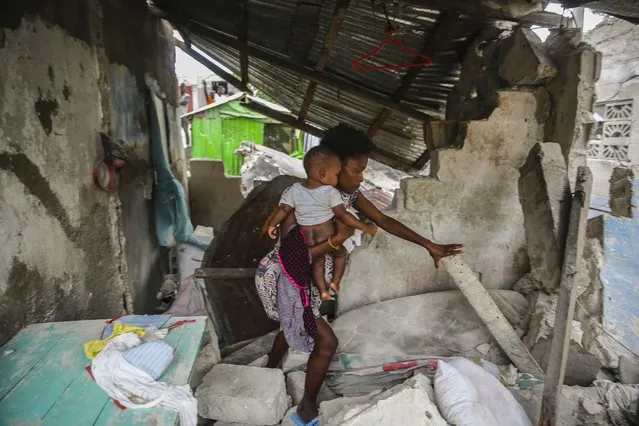 A woman carries her child as she walks in the remains of her home destroyed by Saturday´s  7.2 magnitude earthquake in Les Cayes, Haiti, Sunday, August 15, 2021. (Photo by Joseph Odelyn/AP Photo)