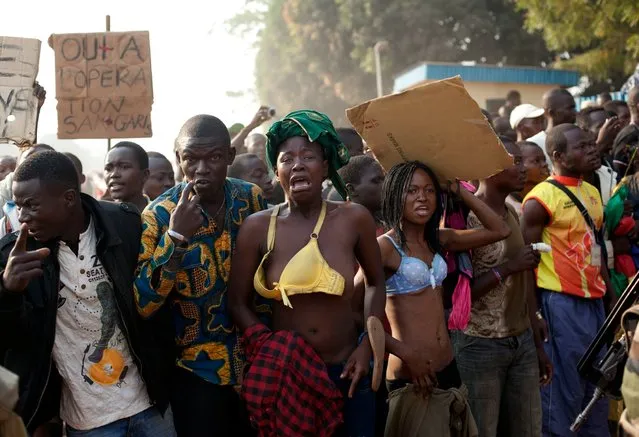 Women bare their chests in a traditional sign of placing a curse, after at least two people were injured by passing Chadian troops, during a protest outside Mpoko Airport in Bangui, Central African Republic, Monday, December 23, 2013. Hundreds of demonstrators gathered at the entrance to the airport Monday morning carrying signs protesting Chadian forces and expressing support for French troops and other regional African forces. At least two people were wounded as pickups of Chadian soldiers sped through the gathered crowd firing off several rounds. (Photo by Rebecca Blackwell/AP Photo)