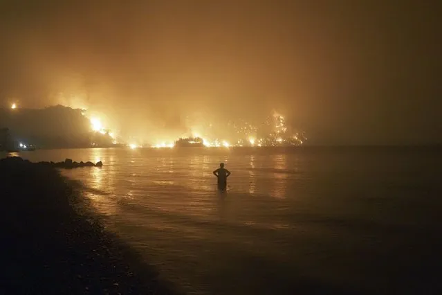 A man watches the flames as wildfire approaches Kochyli beach near Limni village on the island of Evia, about 160 kilometers (100 miles) north of Athens, Greece, late Friday, August 6, 2021. Wildfires raged uncontrolled through Greece and Turkey for yet another day Friday, forcing thousands to flee by land and sea, and killing a volunteer firefighter on the fringes of Athens in a huge forest blaze that threatened the Greek capital's most important national park. (Photo by Thodoris Nikolaou/AP Photo)