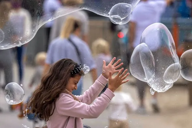 A girl reaches for bubbles near the Santa Monica Pier as crowds gather on Memorial Day as shutdowns are relaxed more than a year after Covid-19 pandemic shutdowns began, in Santa Monica, California on May 31, 2021. (Photo by David McNewAFP Photo)