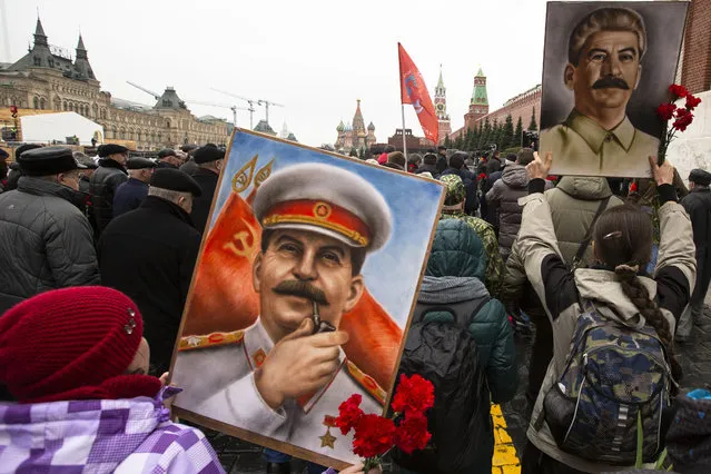 Communist party supporters carry red flags and portraits of Josef Stalin as they walk to place flowers at his grave to mark the 66th anniversary of his death in Red Square, with St. Basil's Cathedral, center, and the Spasskaya Tower, center right, in the background in Moscow, Russia, Tuesday, March 5, 2019. Josef Stalin led the Soviet Union from 1924 until his death in 1953. (Photo by Pavel Golovkin/AP Photo)
