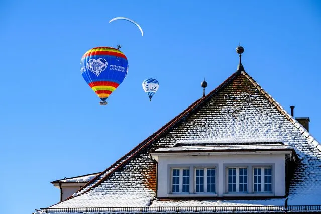 A hot-air balloon flies over houses during the 44th International Hot Air Balloon Festival in Chateau-d'Oex, Switzerland, Saturday, January 20, 2024. (Photo by Jean-Christophe Bott/Keystone via AP Photo)