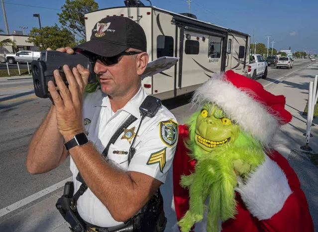 In this photo provided by the Florida Keys News Bureau, Monroe County Sheriff's Office Colonel Lou Caputo, right, costumed as the Grinch, watches Sgt. Greg Korzan, left, as he uses a laser speed detector to check speeds of motorists traveling through a school zone on the Florida Keys Overseas Highway Tuesday, December 13, 2022, in Marathon, Fla. For drivers slightly speeding through the area, Caputo offers them the choice between an onion or a traffic citation. (Photo by Andy Newman/Florida Keys News Bureau via AP Photo)