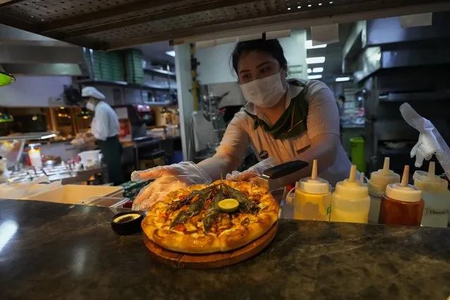 A staff member prepares to serve a pizza topped with a cannabis leaf to the customers at a restaurant in Bangkok, Thailand on November 24, 2021. The Pizza Company, a Thai major fast food chain, has been promoting its “Crazy Happy Pizza” this month, an under-the-radar product topped with a cannabis leaf. It’s legal but won’t get you high. The “Crazy Happy Pizza” is a mashup of toppings evoking the flavors of Thailand’s famous Tom Yum Gai soup along with a deep-fried cannabis leaf on top. Cannabis is also infused into the cheese crust and there's chopped cannabis in the dipping sauce. A 9-inch pie costs 499 baht (about $15). Customers preferring a do-it-yourself variety can choose their own toppings, with a 100 baht ($3) surcharge for two or three cannabis leaves. (Photo by Sakchai Lalit/AP Photo)