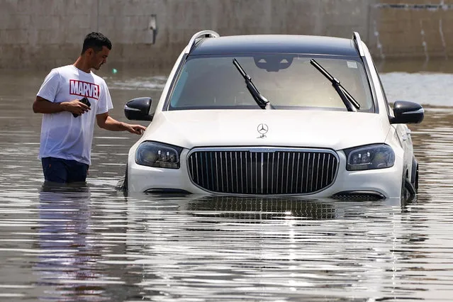 A man stands next to a car partially submerged by flood water following heavy rainfall, in Dubai, United Arab Emirates, on April 19, 2024. (Photo by Amr Alfiky/Reuters)