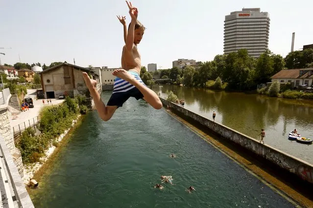 A boy jumps during hot temperatures from a bridge into the Limmat river in Zurich July 3, 2015. On the right is the Sihl river and the headquarters of Swiss retailer Migros. (Photo by Arnd Wiegmann/Reuters)