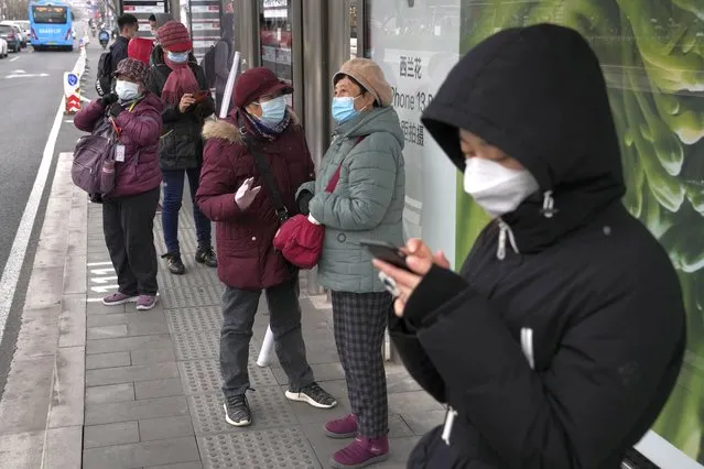 Residents wearing masks chat at a bus stop on Thursday, March 17, 2022, in Beijing. Even as authorities lock down cities in China's worst outbreak in two years, they are looking for an exit ramp from what has been a successful but onerous COVID-19 prevention strategy. (Photo by Ng Han Guan/AP Photo)