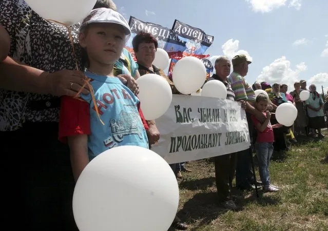 People take part in a commemoration ceremony at the site of the Malaysia Airlines flight MH17 plane crash near the village of Hrabove in Donetsk region, Ukraine, July 17, 2015. The banner reads, “You were killed and they continue to kill us”. (Photo by Igor Tkachenko/Reuters)