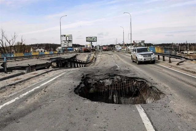 A vehicle drives past a hole on a damaged bridge, in the outskirts of Kyiv on April 8, 2022. (Photo by Ronaldo Schemidt/AFP Photo)