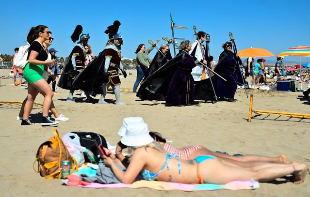 A priest surrounded by female penitents of “Cristo Salvador” (Christ the Saviour) brotherhood walk past sunbathers lying in the sun during the Good Friday procession celebrated on the beach in Valencia on April 7, 2023. Spain's colourful Holy Week celebrations this year began on April 2 – Palm Sunday – featuring centuries-old processions of the faithful carrying flower-covered floats topped with statues of Christ or the Virgin Mary that draw huge crowds. Organised by various religious brotherhoods, the parades are held across the country in the week leading up to Easter Sunday, which this year in the Christian Church falls on April 9. (Photo by Jose Jordan/AFP Photo)