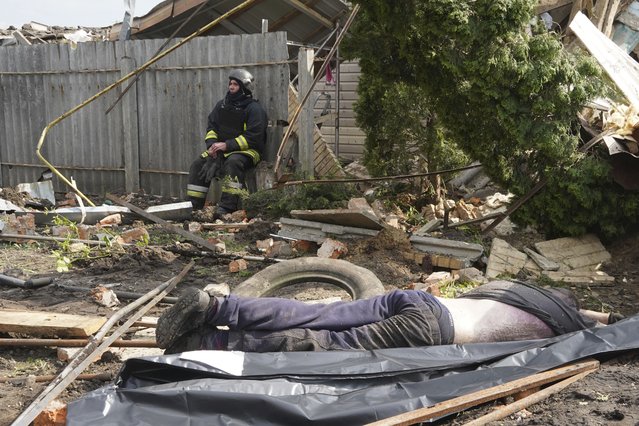 A rescue worker sits in front of a body of a local resident who was killed by Russian rocket attack in Tsyrkuny, Ukraine, Thursday, May 18, 2023. (Photo by Andrii Marienro/AP Photo)