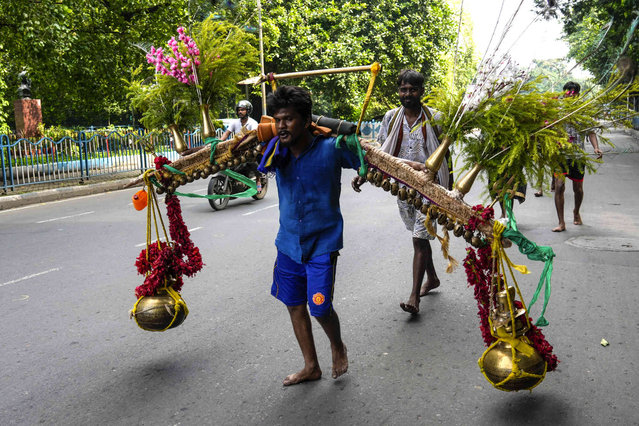 A Hindu devotee carries two huge pots of holy water from the Hooghly River to offer it in a temple of Hindu god Shiva during “Shravan Somwar”, the last Monday of the Hindu calendar month Shravan, Hindus consider auspicious in Kolkata, India, Monday, August 12, 2024. (Photo by Bikas Das/AP Photo)