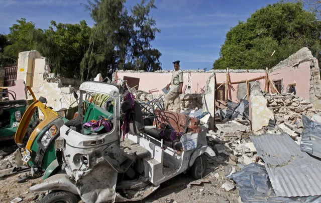 A member of Somalia's security forces walks past destroyed vehicles at the scene of a car bomb blast and gun battle targeting a restaurant in Mogadishu, Somalia Thursday, June 15, 2017. Somali survivors early Thursday described harrowing scenes of the night-long siege of a popular Mogadishu restaurant by al-Shabab Islamic extremists that was ended by security forces. (Photo by Farah Abdi Warsameh/AP Photo)