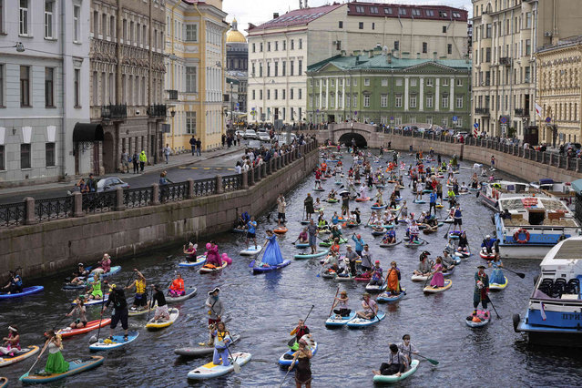 People steer their stand-up paddle (SUP) boards along Moyka River during annual costumed 'Fontanka' SUP-boards festival in St. Petersburg, Russia, Saturday, August 3, 2024. (Photo by Dmitri Lovetsky/AP Photo)