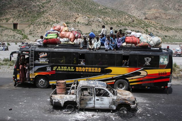 A bus with passengers sitting on the roof with belongings, drives past a damaged vehicle, a day after separatist militants conducted deadly attacks, in Bolan district of Pakistan's restive province of Balochistan, Pakistan on August 27, 2024. (Photo by Naseer Ahmed/Reuters)