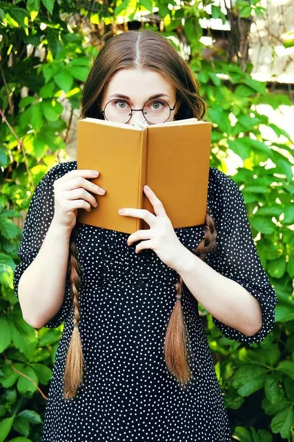 Young student woman with glasses wearing black dress with white dots with long braids waiting holding a romance novel. Retro fashion. (Photo by 
Nata Nytiaga/Getty Images)