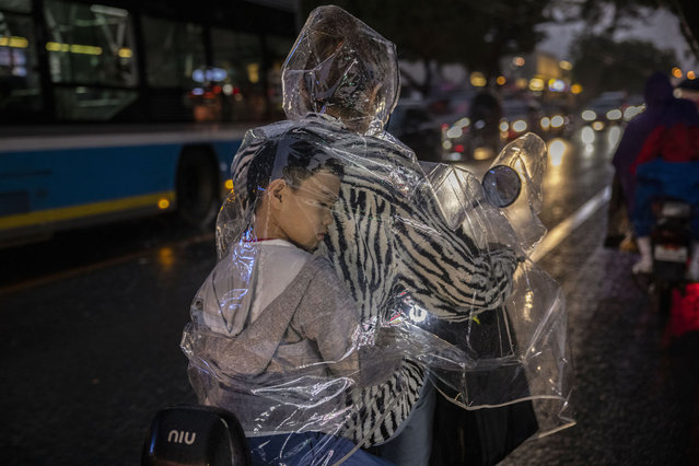 A boy sits inside his mother's plastic raincoat as they ride on a scooter during a rainstorm on September 8, 2021 in Beijing, China. While cases were relatively low compared to many countries, China has recently contained a COVID-19 outbreak of the highly contagious Delta variant. (Photo by Kevin Frayer/Getty Images)