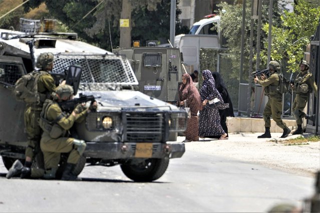 Israeli soldiers escort female relatives of a wanted Palestinian man out of his besieged house in the West Bank Town of Urif, Thursday, June 29, 2023. The Israeli military entered the town of Urif in the northern West Bank on Thursday and surrounded the house of a wanted Palestinian, sparking clashes with residents protesting the incursion. (Photo by Majdi Mohammed/AP Photo)