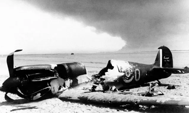 A British Spitfire fighter lays with its cockpit blasted out, after it crashed to the beach at Dunkirk, France on June 6, 1940, the last stand port of the Allied forces which fled from Flanders. Smoke from burning Dunkirk may be seen in the background. (Photo by AP Photo)