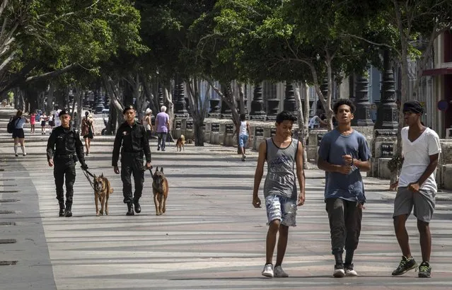 People walk at the Paseo del Prado while members of the police patrol in Havana, Cuba, Monday, July 11, 2022. A year after the largest protests in decades shook Cuba's single-party government, the economic and political factors that caused them largely remain. (Photo by Ramon Espinosa/AP Photo)