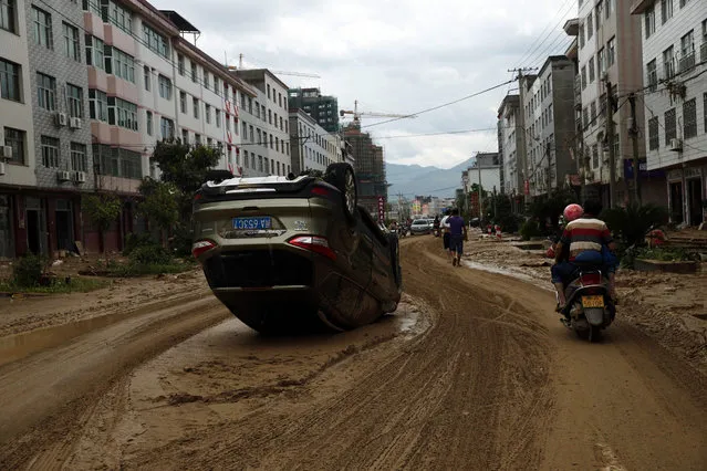 This photo taken on July 10, 2016 shows residents riding a motorbike past an overturned car in the aftermath of a tropical storm in Bandong town, in Minqing county, east China's Fujian province. A tropical storm that made landfall in Fujian province on July 9 left six people dead and at least eight more missing, reports said, after it lashed Taiwan with typhoon-grade winds and rain. (Photo by AFP Photo/Stringer)