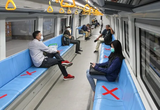 People sit on designated areas decided by red cross marks to ensure social distancing inside a light rapid transit train in Palembang, South Sumatra on March 20, 2020, amid concerns of the COVID-19 coronavirus outbreak. (Photo by Abdul Qodir/AFP Photo)