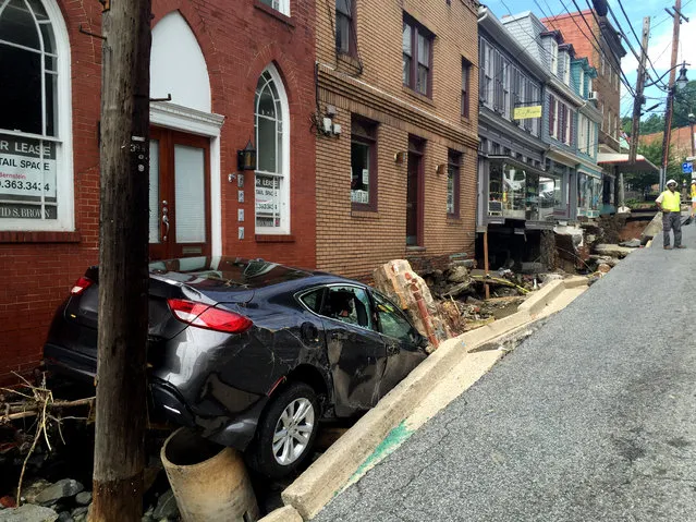 Workers gather by the sidewalk of Main Street that caved in after Saturday night's flooding in Ellicott City, Md., Sunday, July 31, 2016. Historic, low-lying Ellicott City, Maryland, was ravaged by floodwaters Saturday night, killing a few people and causing devastating damage to homes and businesses, officials said. (Photo by Kevin Rector/The Baltimore Sun via AP Photo)