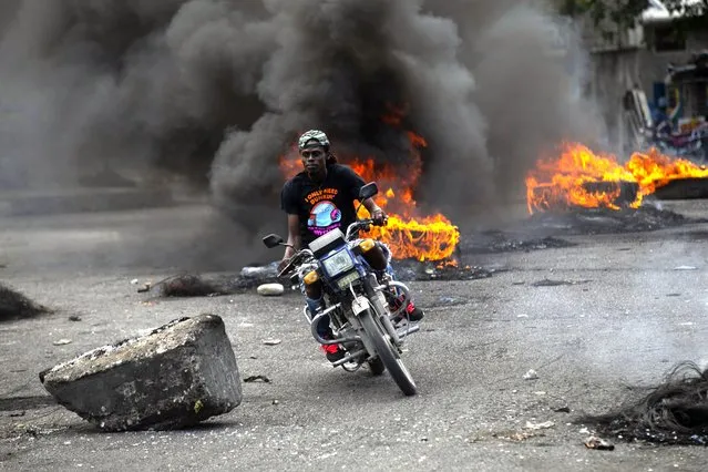 A moto-taxi driver rides past a burning barricade set up by demonstrators protesting fuel price hikes and demanding Haitian Prime Minister Ariel Henry step down in Port-au-Prince, Haiti, Monday, September 26, 2022. (Photo by Joseph Odelyn/AP Photo)
