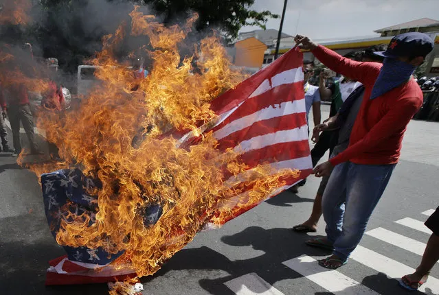 Protesters burn a U.S. flag during a rally near the venue of ASEAN summit and meetings in Manila, Philippines on Sunday November 12, 2017. The group is protesting against the visit of U.S. President Donald Trump, who is currently on a trip to Asia with the Philippines as his last stop for the ASEAN leaders' summit and related summits between the regional grouping and its Dialogue Partners. (Photo by Aaron Favila/AP Photo)
