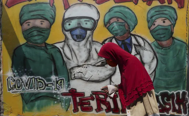 A woman wears a face mask to help curb the spread of the new coronavirus past a coronavirus awareness mural at Rawa Pasung village in Bekasi on the outskirts of Jakarta, Indonesia, Thursday, July 23, 2020. (Photo by Achmad Ibrahim/AP Photo)